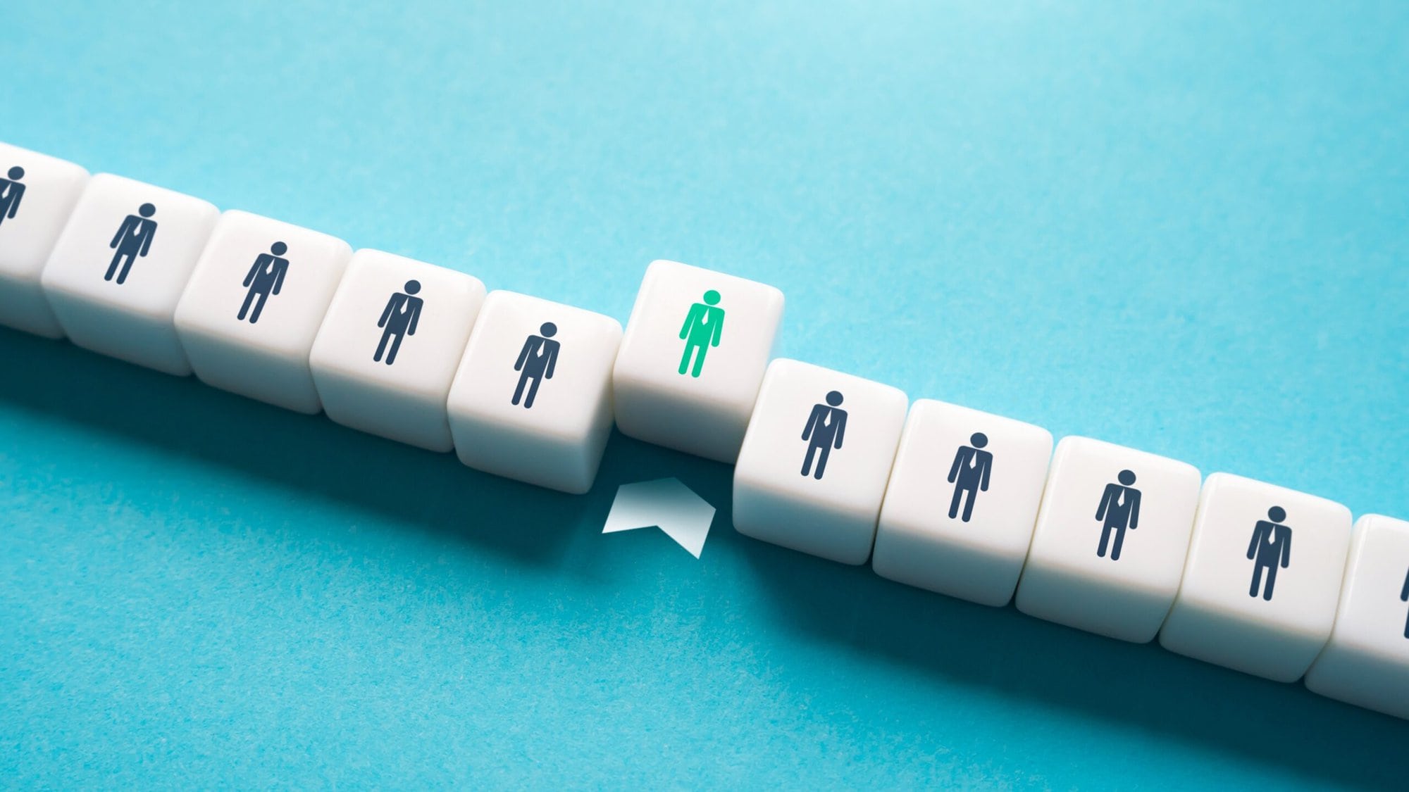 Two parallel rows of white cubes are arranged on a blue background. Each cube features a black icon of a person, except for one in the center with a green person icon. A white arrow points from the bottom row to the top row, directly beneath the green icon, suggesting selection or upward movement. The image conveys themes of individuality, recruitment, or leadership.