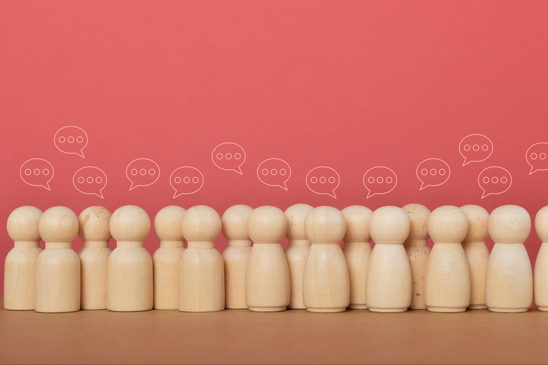A crowd of individual wooden people icons standing together with small speech bubbles above them.